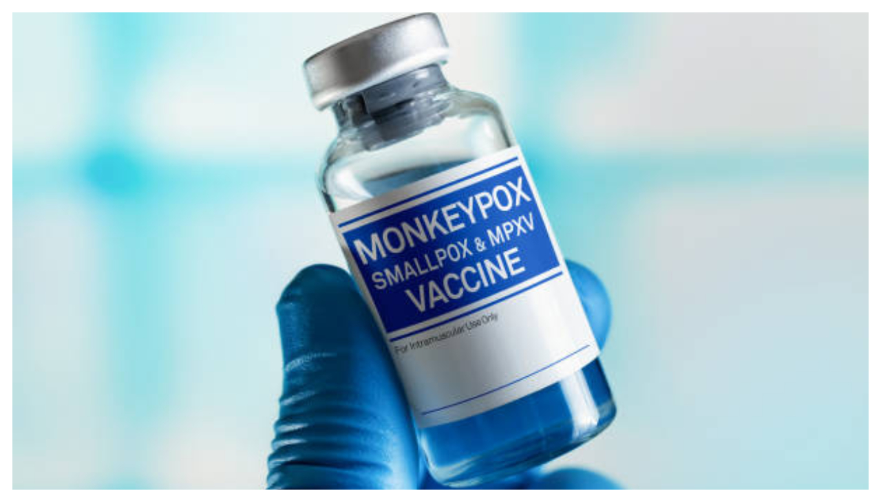 A vial of monkeypox vaccine, held by a blue gloved hand. Text on the vial reads "monkeypox smallpox & MPXV Vaccine"