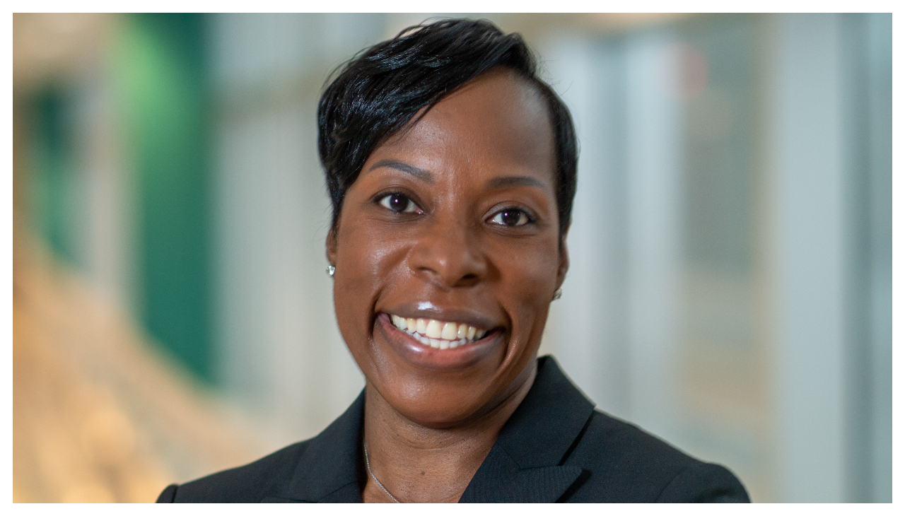 Dr. Chaudron Carter Short, a dark skinned woman with short hair. She is shown from the shoulders up, wearing a black business jacket. She is facing the viewer and is smiling.
