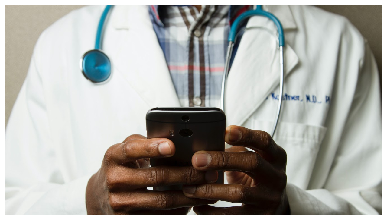 A doctor shown from the neck to the waist, holding a phone he is typing on.