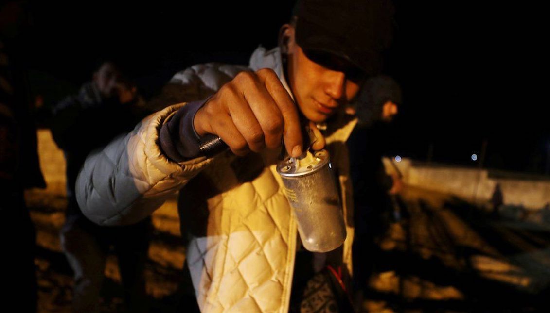An immigrant shows the cameras a can of tear gas on the border with Tijuana. Photo: Reuters